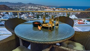 A round glass table with wicker chairs on a balcony overlooking a cityscape with mountains and the sea. - Greatest view in the world! (Cabo San Lucas)