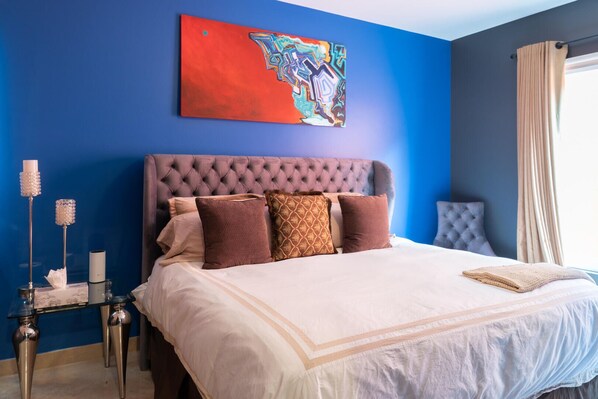 A bedroom with a tufted headboard, a large painting, and a bedside table with candles. - Greatest view in the world! (Cabo San Lucas)
