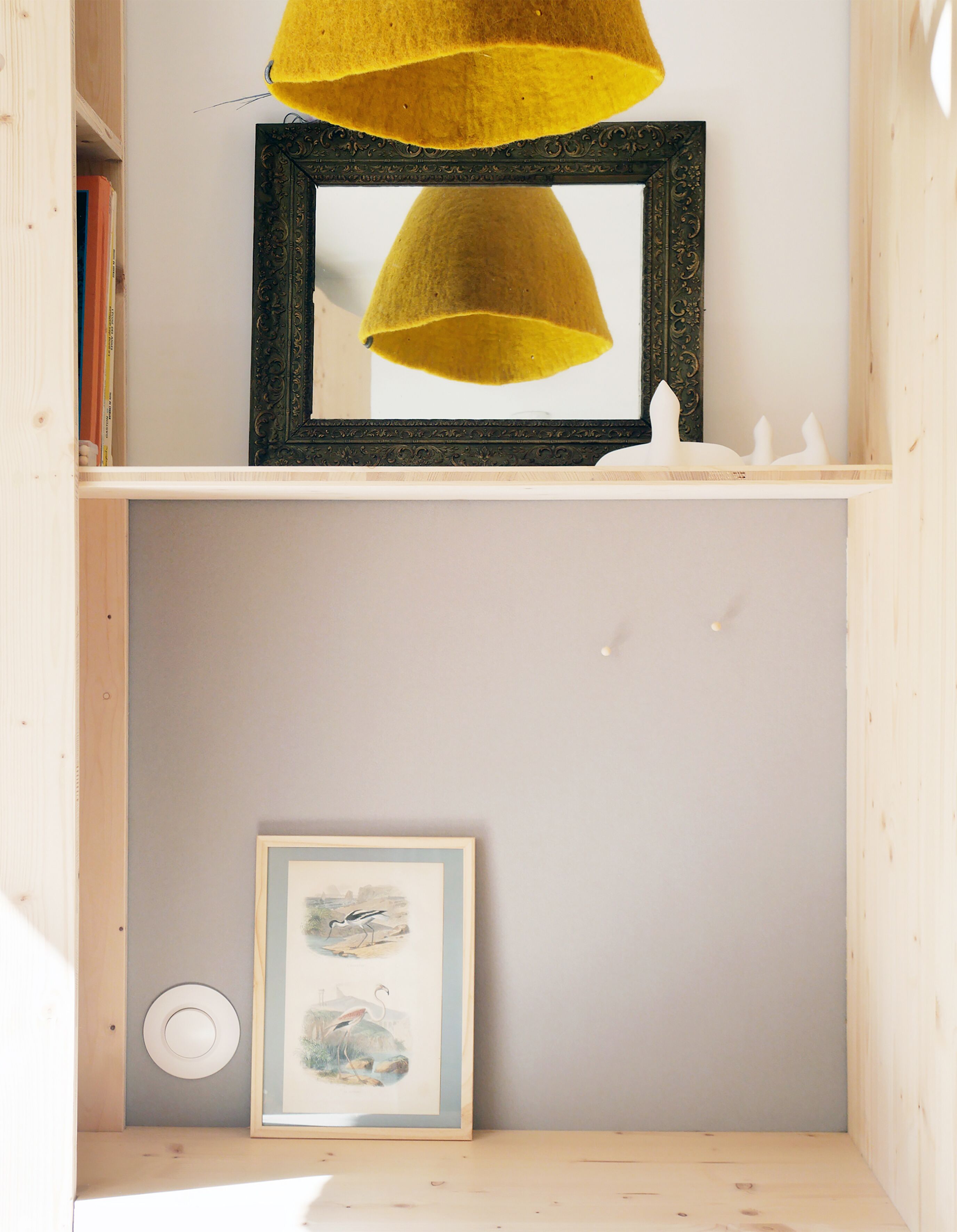A shelf with a framed picture, a yellow lampshade, and a white candle.