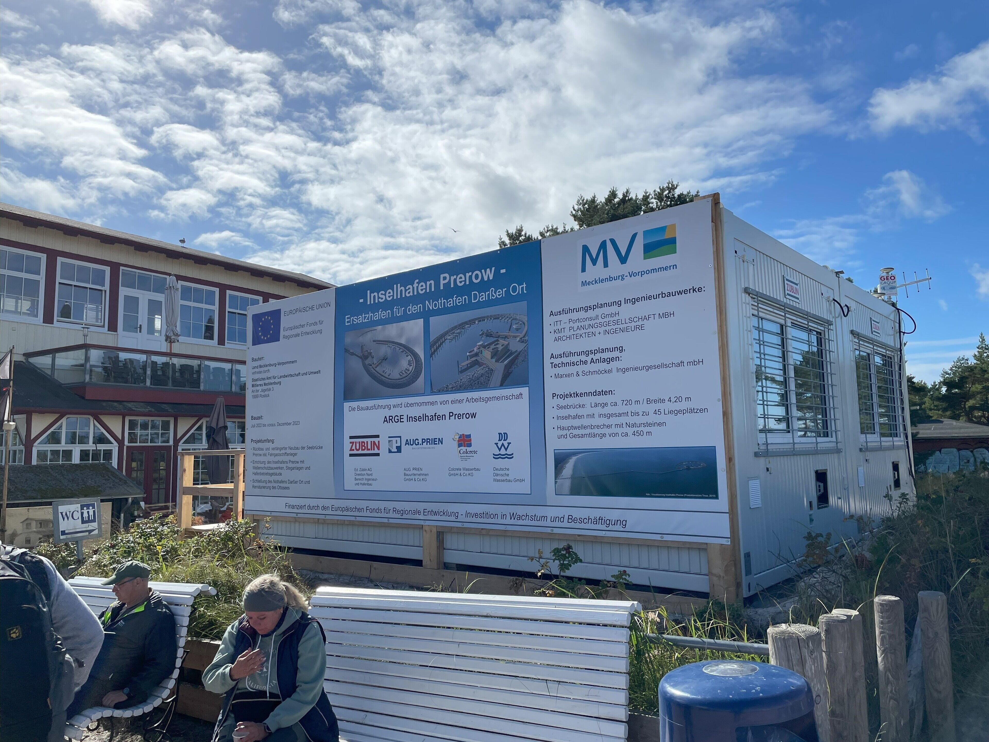 A large informational signboard with text and logos, likely detailing a project or construction site.