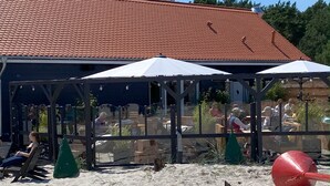 A beachside café with outdoor seating under umbrellas, a red beach ball, and a building with a red-tiled roof in the background. - Right next to the nature reserve! Great for dogs and nature lovers (Prerow)