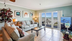 A living room with a sofa, armchairs, a coffee table, a ceiling fan, and a large window with a view of the ocean. - Sea Breeze 106 - Sea, Sun, and Coastal Serenity (Madeira Beach)