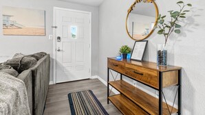 A room with a bed, a wooden console table with a mirror, a small plant, and a framed picture.