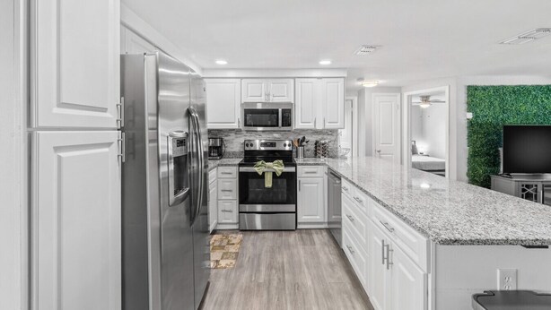 A modern kitchen with white cabinetry, stainless steel appliances, a granite countertop, and a green wall accent.