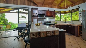 A kitchen with wooden cabinets, a central island, and large windows offering a view of greenery. - Casa Bromelia, 30 minutes from La Fortuna (La Tigra)