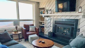 A modern living room with a fireplace, leather armchair, and grey sofas.