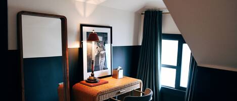 A room with a desk, chair, lamp, framed picture, and a window with curtains.