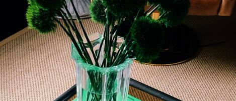 Un jarrón de vidrio transparente con plantas verdes sobre una mesa, una silla de cuero marrón y un libro verde titulado 'SOMETHINGS'.