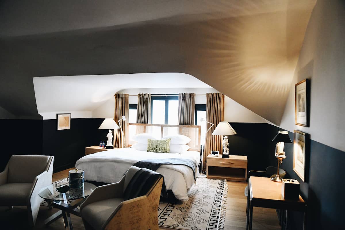 A modern hotel room with a large bed, two bedside tables, a desk, and a chair.