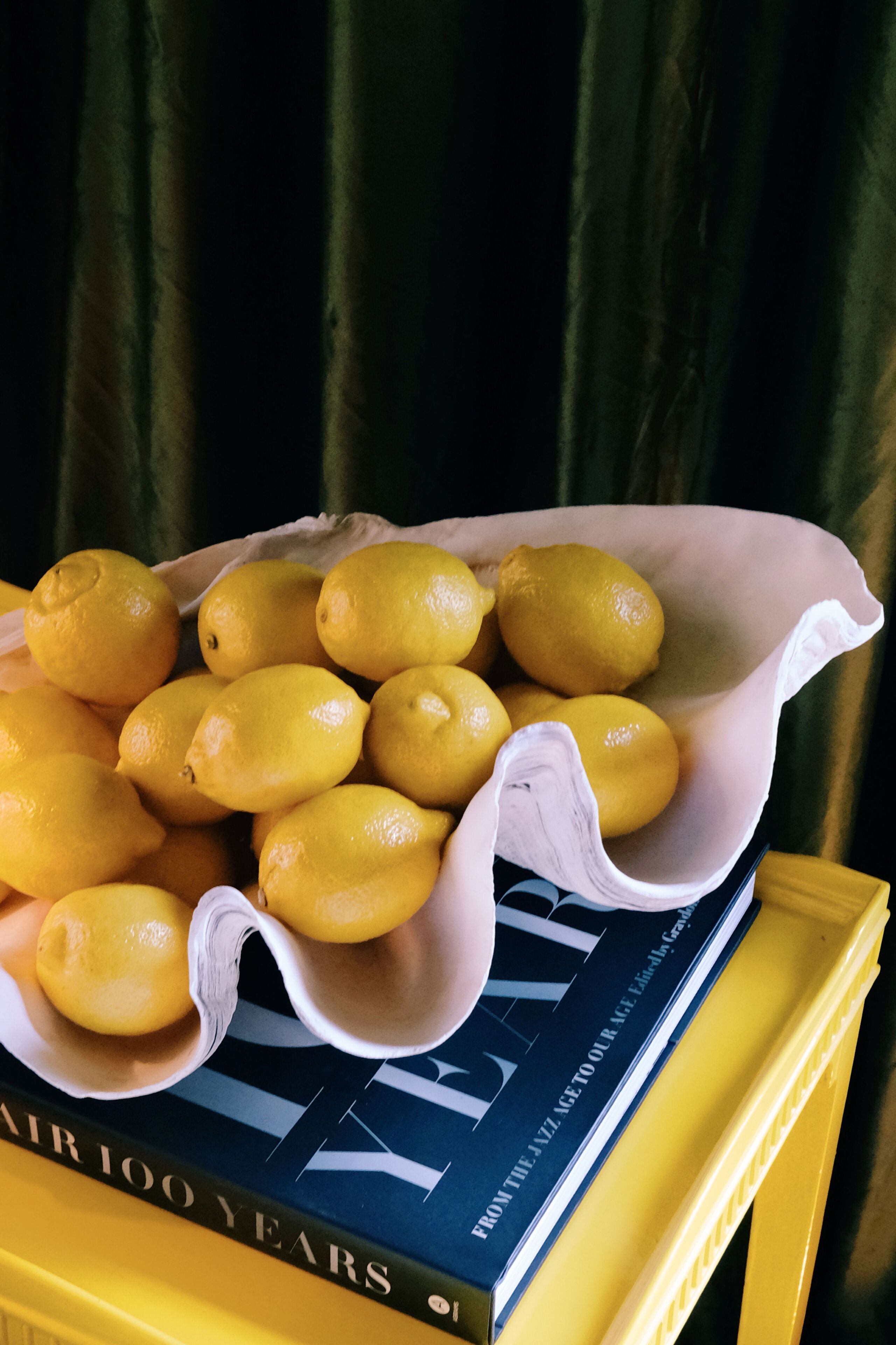 A basket of lemons on a yellow surface with a book titled "AIR 100 YEARS" underneath.
