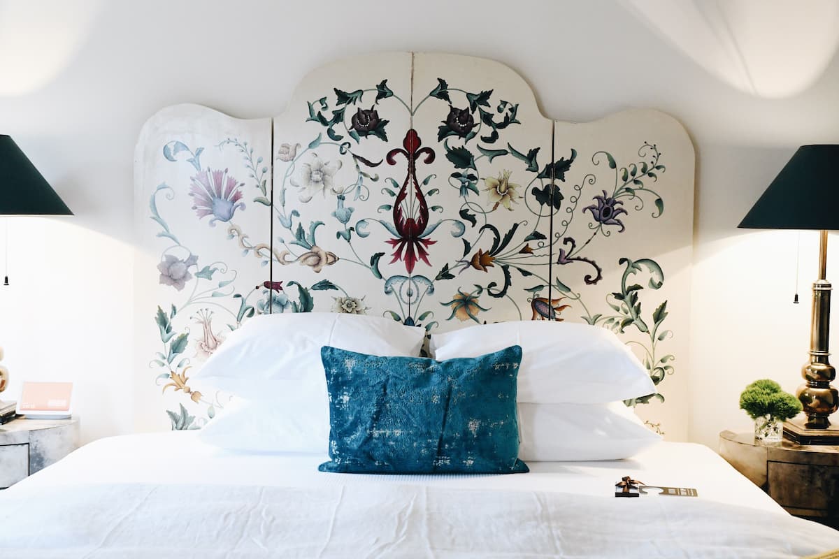 A bed with white linens, a blue decorative pillow, and a floral headboard.