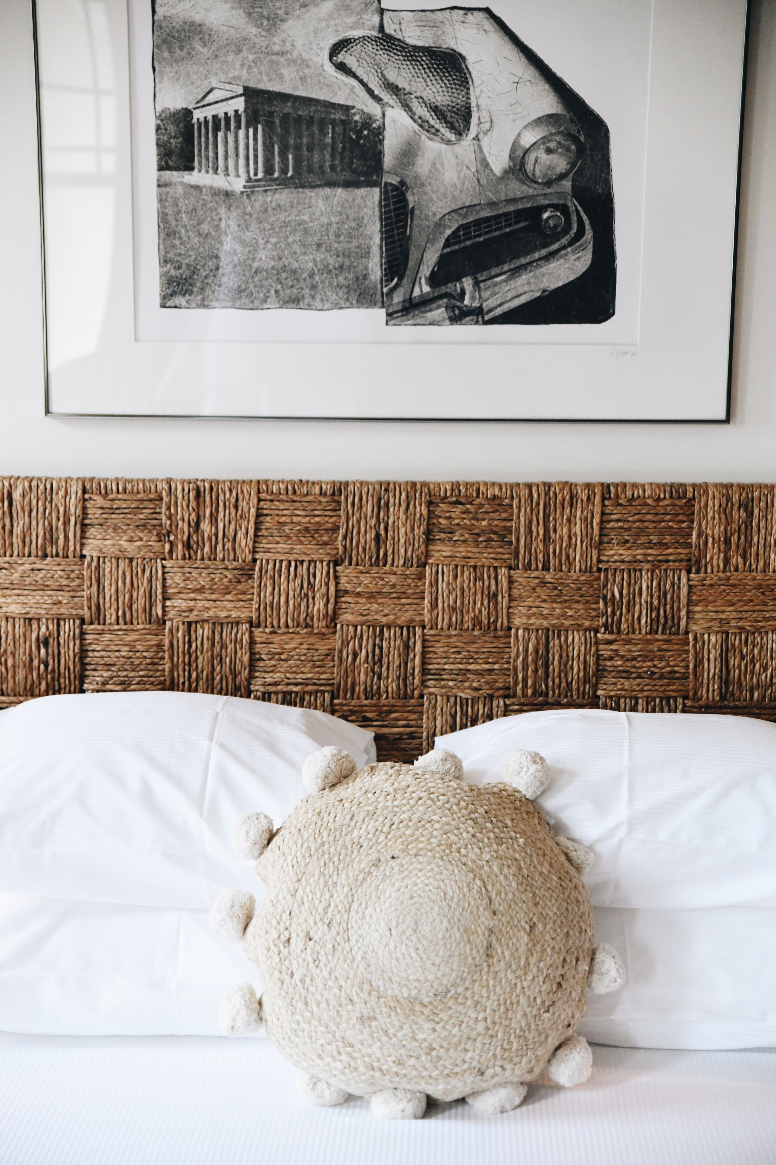A bed with a woven headboard, white pillows, and a knitted pouf.