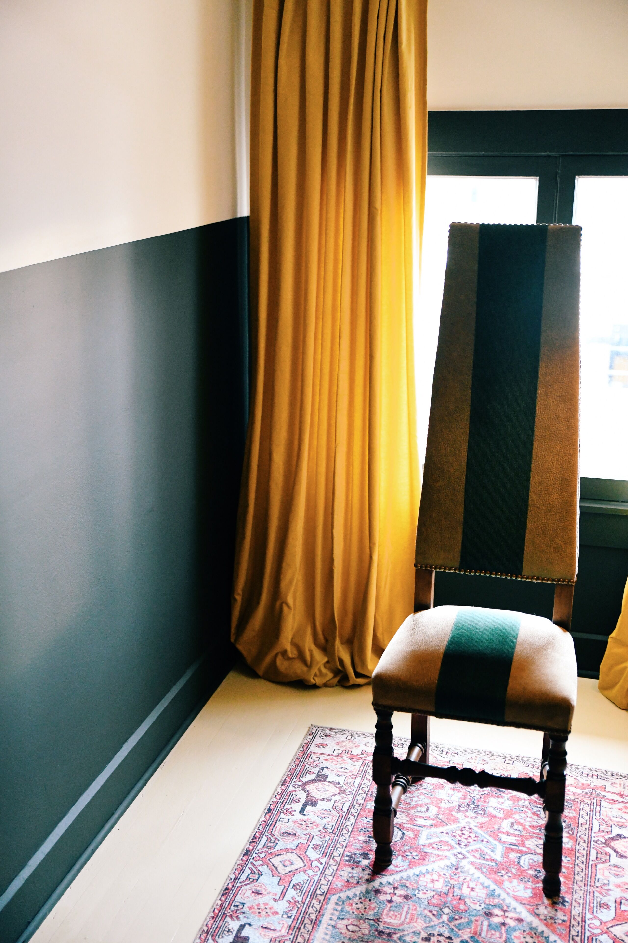 Una habitación con un rug adornado, un sillón con cojín a rayas, y un ventanal con vistas.