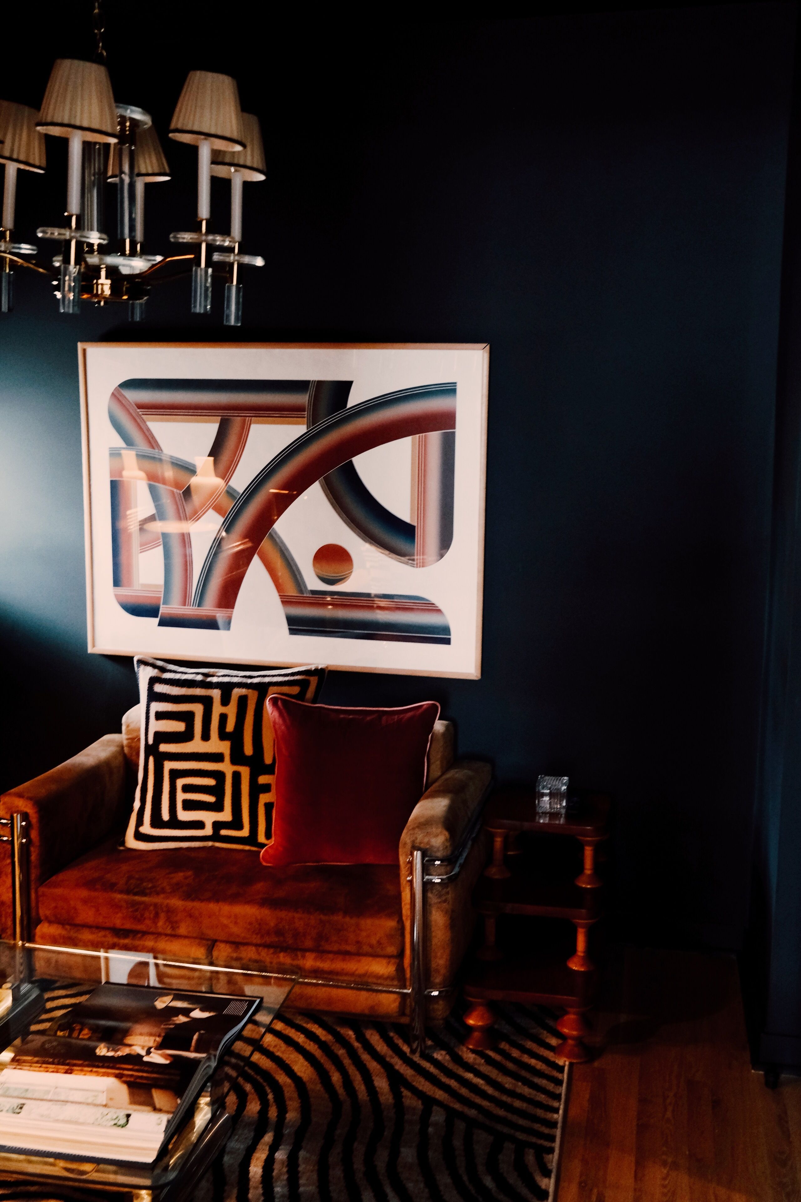 Un salon moderne avec un mur de couleur sombre, une œuvre d’art abstraite encadrée, un canapé en cuir agrémenté de coussins à motifs, une table basse en bois et un tapis à motifs.