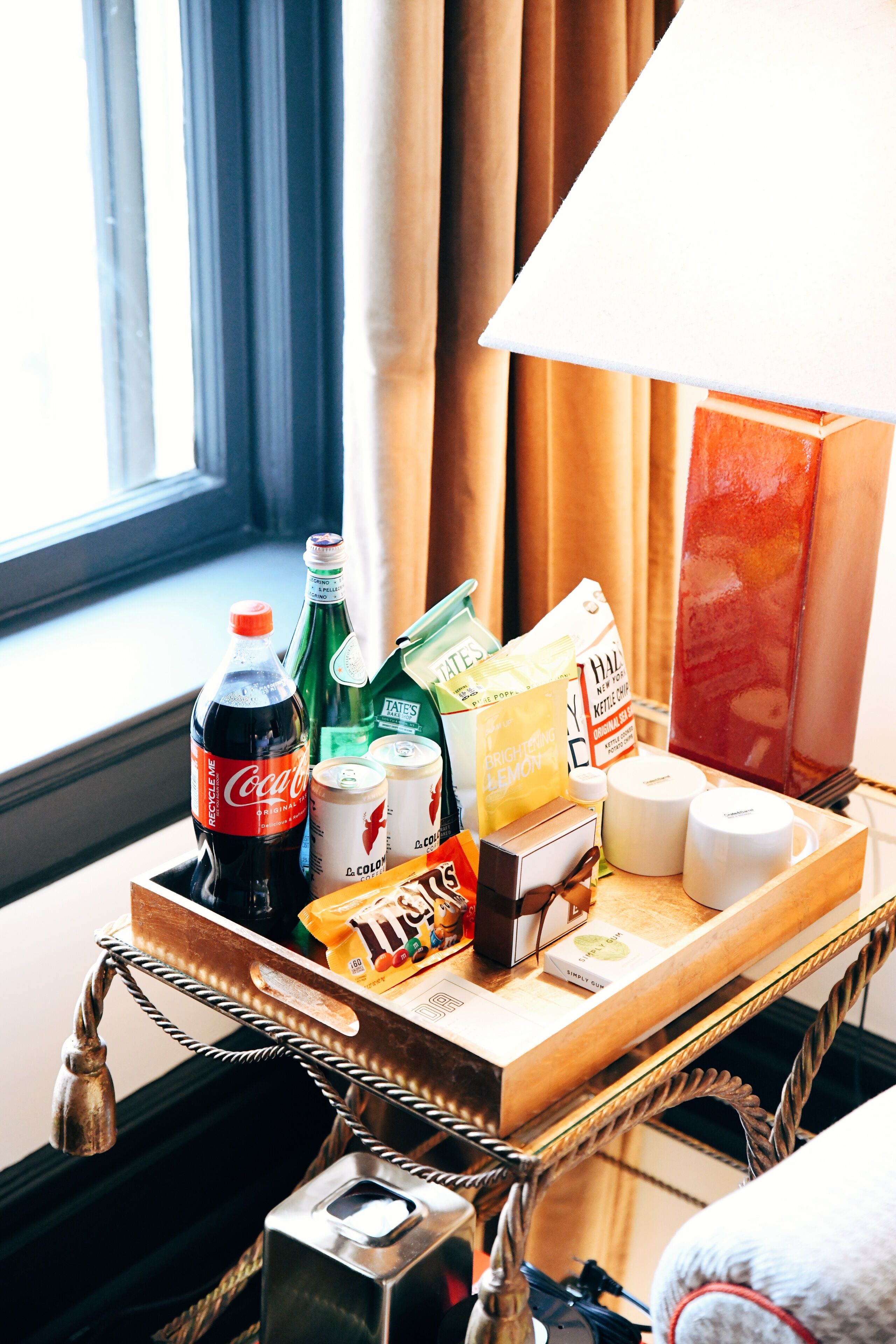 A tray with various items including a bottle of Coca-Cola, a green bottle, a bag of chips, a box of tissues, and a candle.