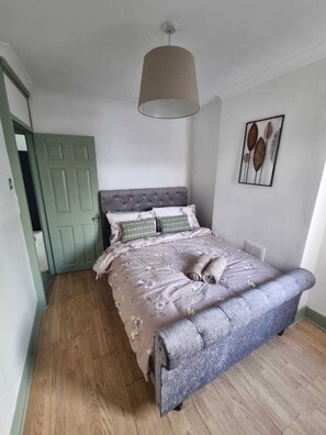 Ein Schlafzimmer mit einem Bett, einer grünen Tür, einer Deckenleuchte und einem Wandbild.