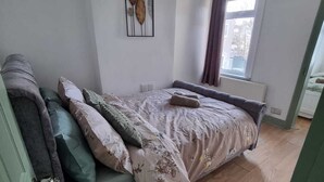 Un dormitorio con cama, ventana con cortinas, radiador y una obra de arte colgada en la pared.