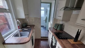 Una cocina moderna con encimera de madera, pileta de acero inoxidable y vista al baño contiguo.