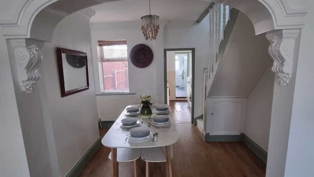 Comedor con una mesa dispuesta para cuatro personas, flanqueado por paredes blancas y suelo de madera.