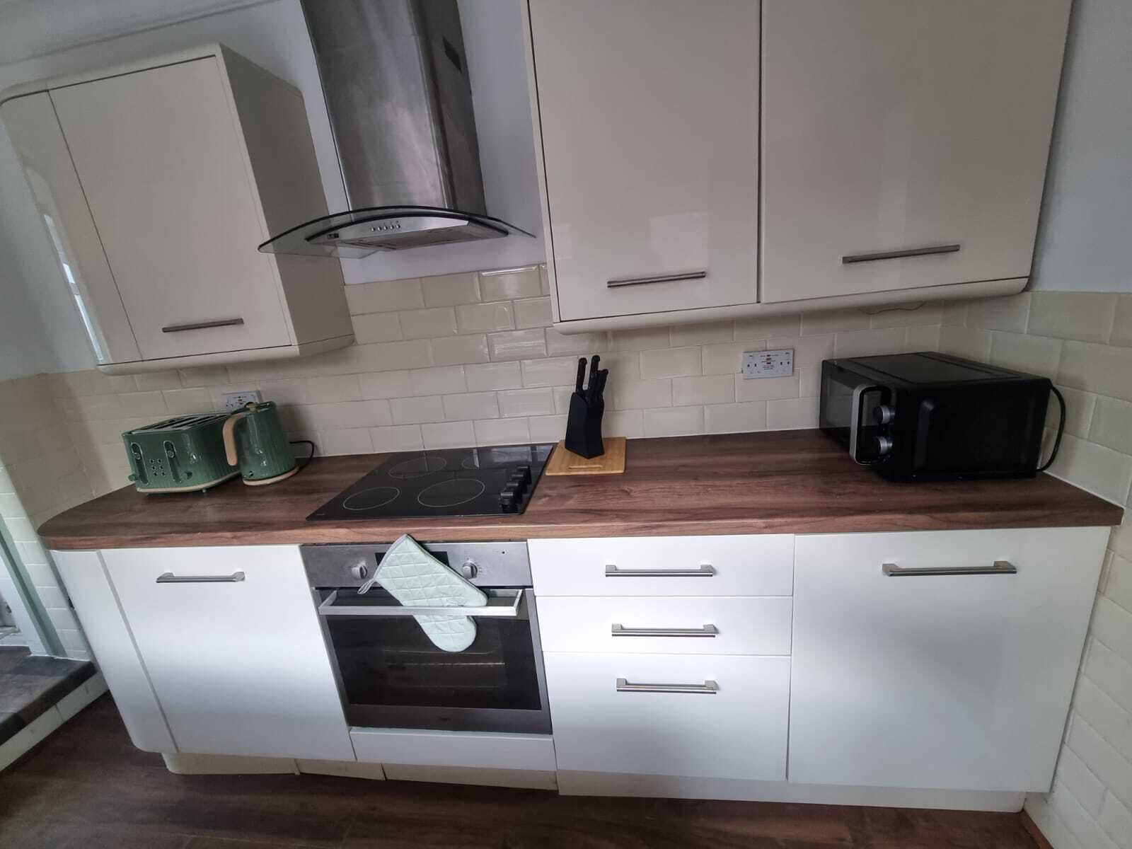 Una cocina con armarios blancos, una campana extractora de acero inoxidable, un microondas y un tostador.