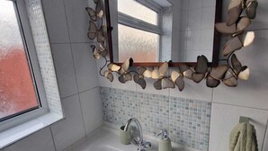 Un baño con un lavamanos blanco, un espejo con marco decorado como hojas, y una ventana.