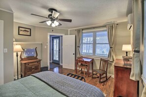 A bedroom with a bed, a desk, a rocking chair, a ceiling fan, and a window with curtains.