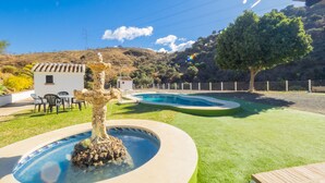 A swimming pool with a decorative fountain, surrounded by a well-maintained lawn and a small patio area with outdoor furniture. - Cubo's Finca La Curva High Privacy / Private pool / Views (Pizarra)