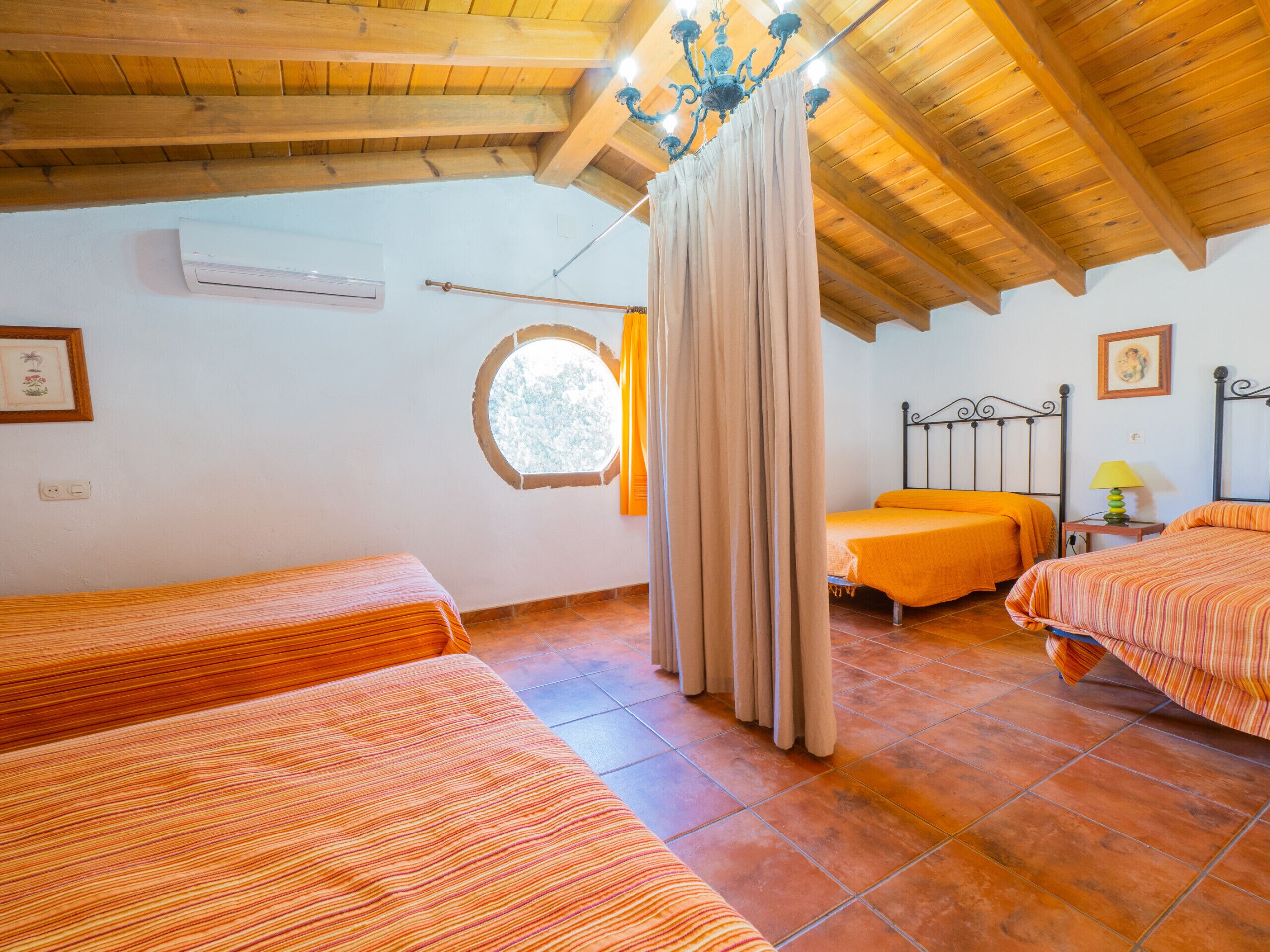 A room with two beds, a window, a chandelier, and a bed with a curtain.
