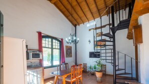 A dining area with a wooden table and chairs, a kitchen with a microwave, and a staircase with a metal railing. - Cubo's Finca La Curva High Privacy / Private pool / Views (Pizarra)