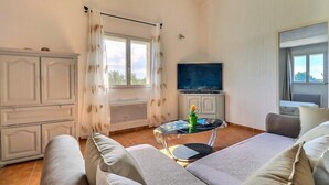Ett rum med en soffa, ett litet bord med en vas, en tv och ett fönster med gardiner.