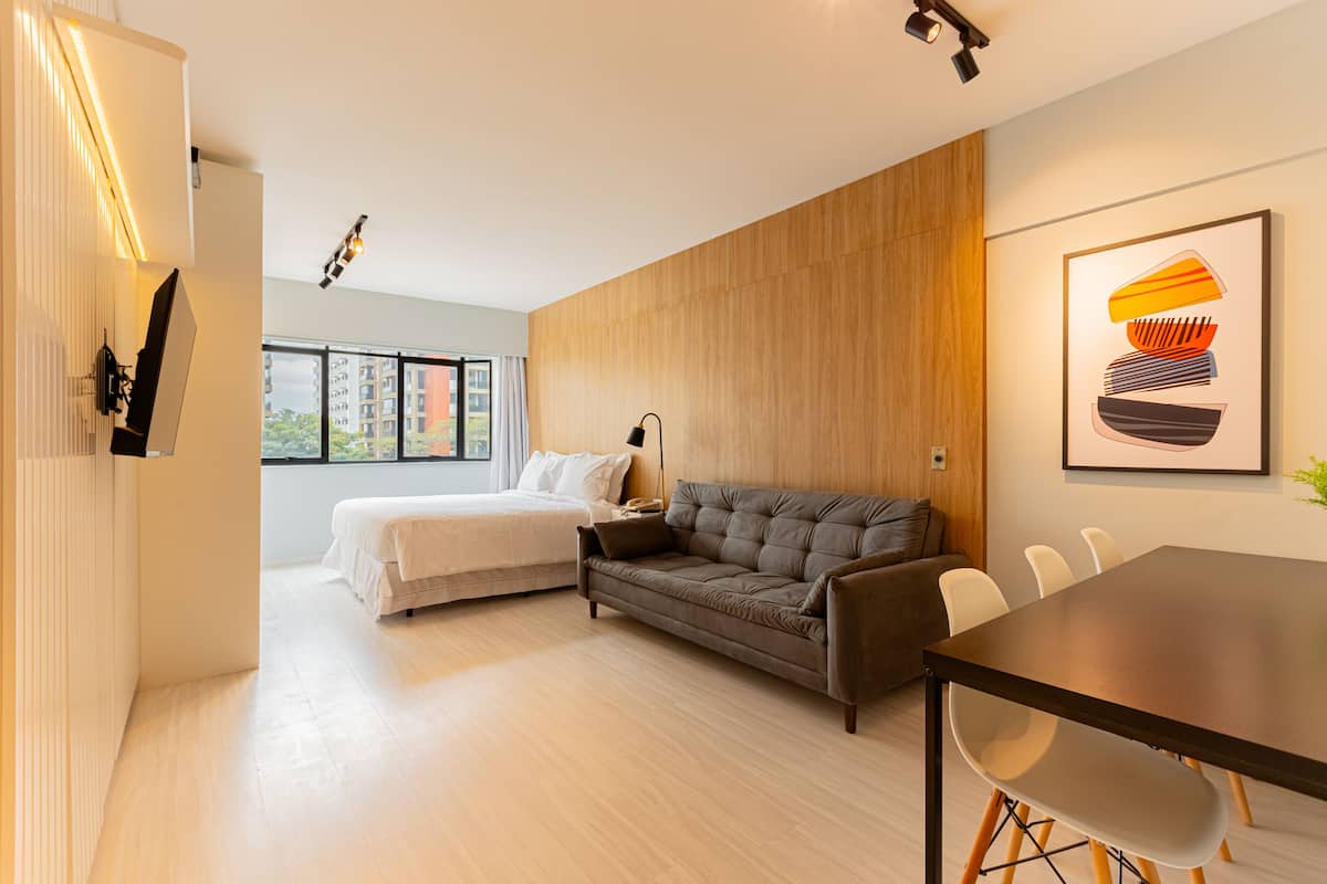 Habitación de hotel moderna con cama, sofá, mesa de comedor y un amplio ventanal con vistas a la ciudad.