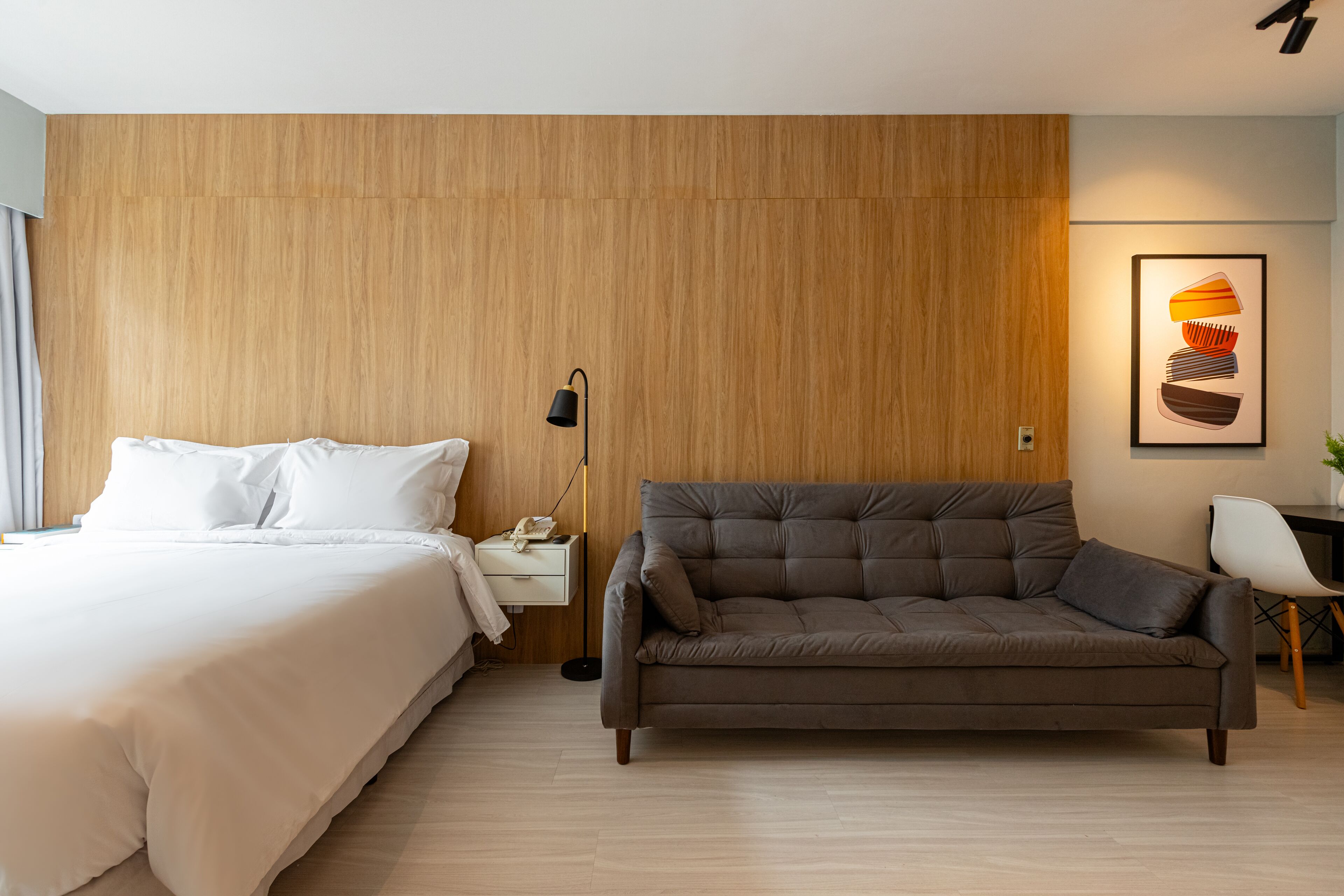 Ein modernes Hotelzimmer mit Bett, einer Couch, einem Nachttisch mit Lampe und einem Wandbild.