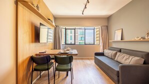 Una sala de estar moderna con una pared de madera, un sofá, una mesa de comedor con sillas y un ventanal con cortinas.