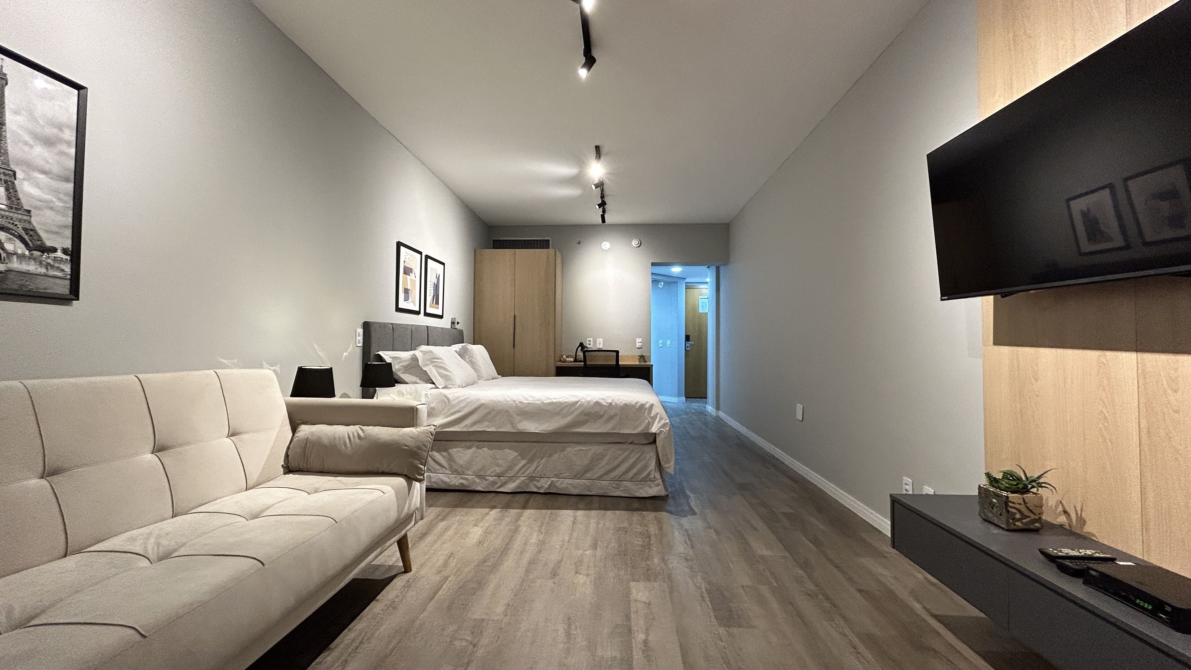 A modern hotel room with a sofa, bed, flat-screen TV, and a wooden desk.
