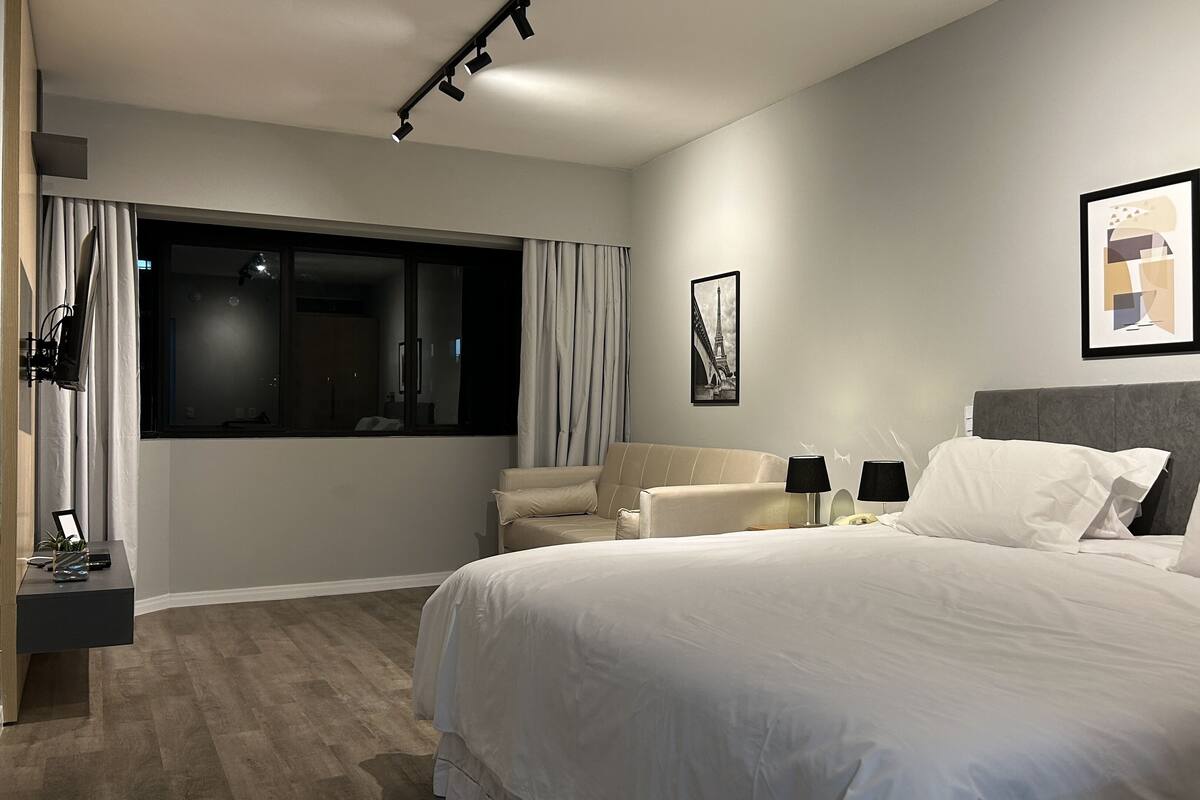 Una habitación de hotel moderna con una cama grande, una zona de estar con sofá, un escritorio con lámpara y obras de arte en las paredes.