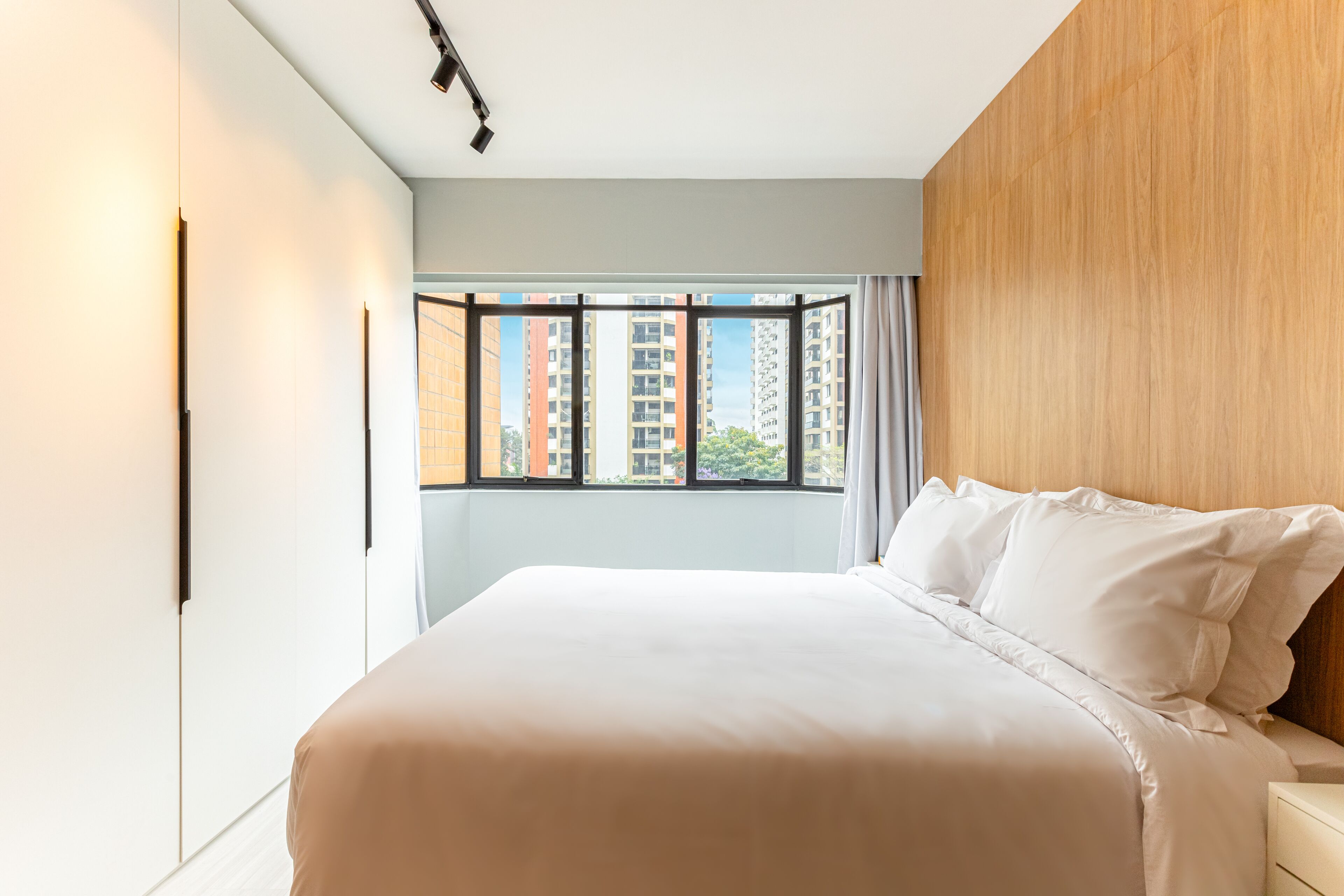 Un dormitorio moderno con una cama grande, una ventana con cortinas y vistas a rascacielos.