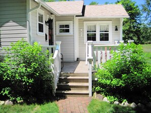 A two-story house with a front porch, a set of stairs leading to the entrance, and a small garden area with bushes.