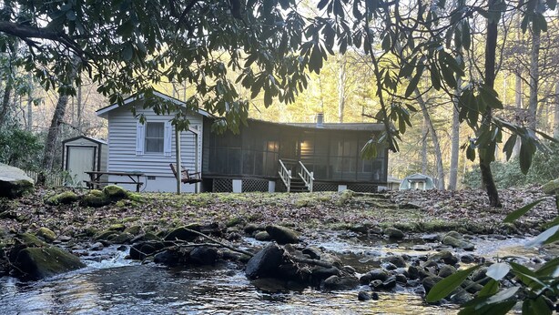 Eine rustikale Holzhütte mit Veranda, umgeben von Wald und einem kleinen Bach.