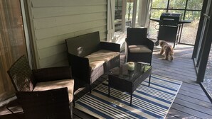 Ein überdachter Balkon mit Korbmöbeln, einem Glastisch und einer Streifenoptik-Perser.