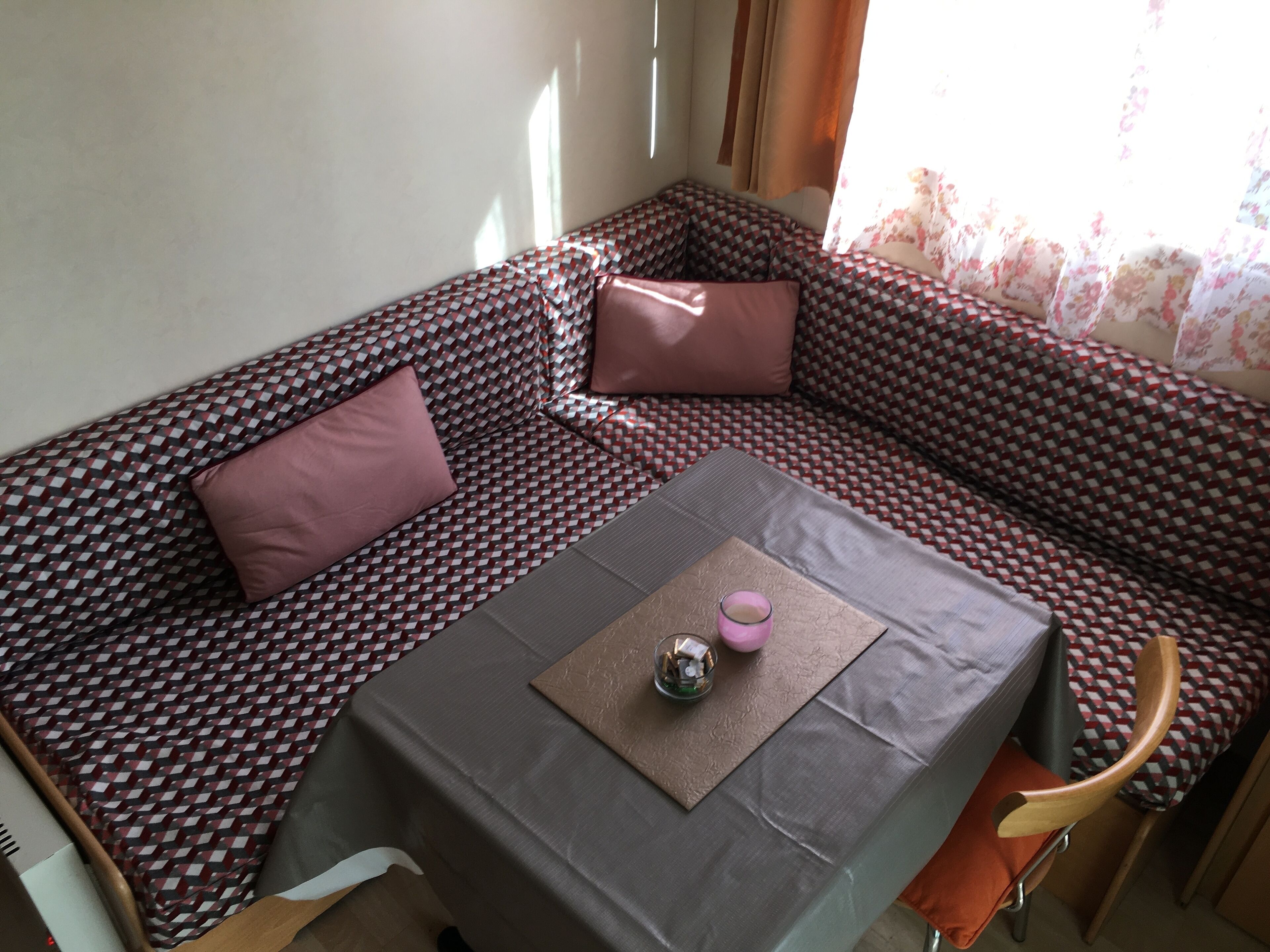 A cozy room with a patterned sofa, a small table with a glass and a pink object, and a chair.