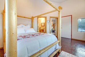 A four-poster bed with a white bedspread and floral pattern, wooden beams, a wooden floor, a window with a view, and a door leading to another room. - Scenic Great Falls Retreat On Missouri River! (Great Falls)
