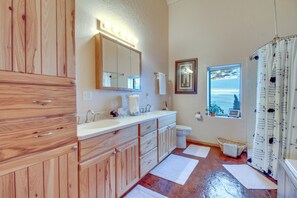 A bathroom with wooden cabinets, a vanity with a mirror, a toilet, and a window with a view of a snowy landscape. - Scenic Great Falls Retreat On Missouri River! (Great Falls)