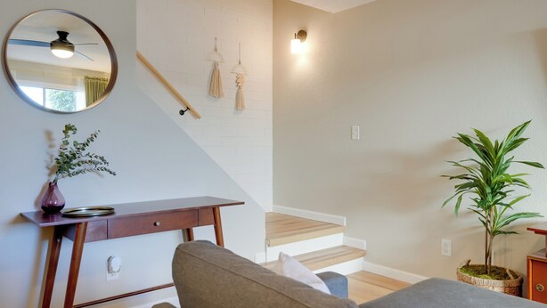 A modern living room with a wooden desk, a round mirror, a staircase, and a potted plant. - 2 Mi to Old Town: Home w/ Pool Access & Patio (Scottsdale)