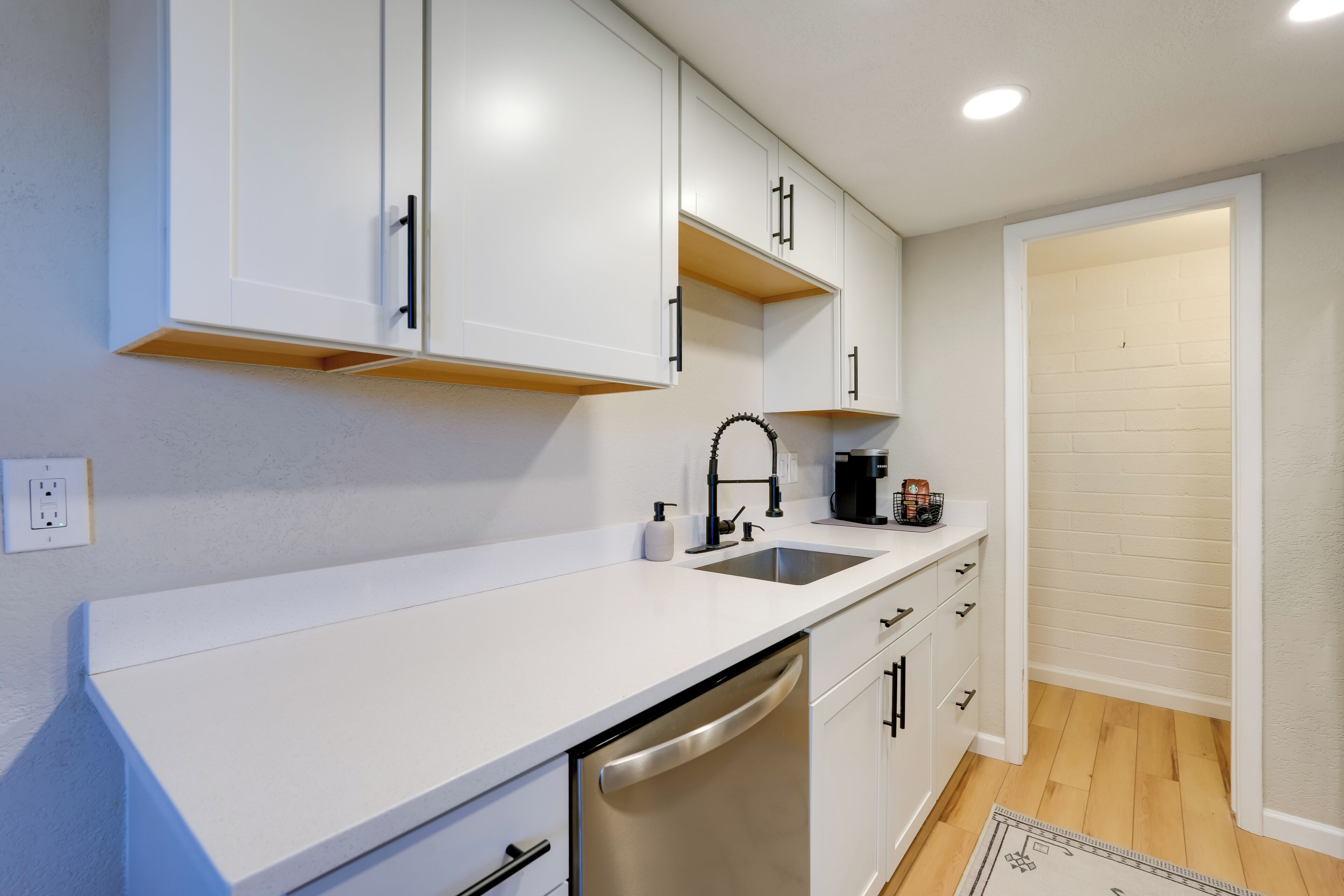 A modern kitchen with white cabinets, a stainless steel dishwasher, and a sink.