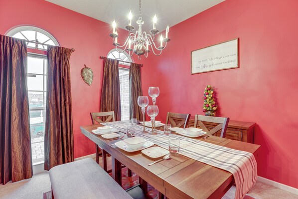 Comedor con una mesa de madera dispuesta para cuatro personas, una araña y una pared roja con una cita enmarcada.