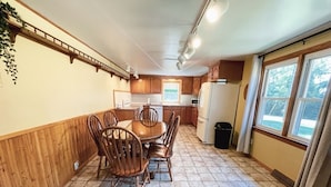 Une cuisine compacte comprenant une table et des chaises, des meubles en bois, un réfrigérateur et une fenêtre avec des rideaux.