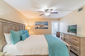 A bedroom with a bed, a ceiling fan, a painting, a television, and a window with blinds.