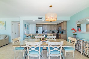 A spacious kitchen with modern appliances, a dining area with wooden chairs and a glass table, and a light blue color scheme. - Solace-Edgewater 613T3 Beachfront-Fully Renovated! Luxurious Walk-In Shower! (Panama City Beach)
