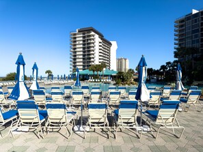 Ein Poolbereich mit Liegestühlen und Sonnenschirmen, bewölkter Himmel und ein hohes Gebäude im Hintergrund.