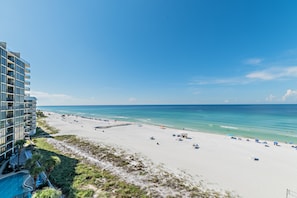 A beach with a hotel building on the left, clear skies, and calm sea. - Solace-Edgewater 613T3 Beachfront-Fully Renovated! Luxurious Walk-In Shower! (Panama City Beach)